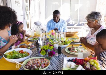 Multiracial multigeneration family with meal on table praying before having lunch at dining table Stock Photo