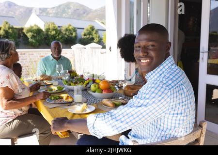 Portrait of smiling young man having lunch with multiracial multigeneration family at dining table Stock Photo