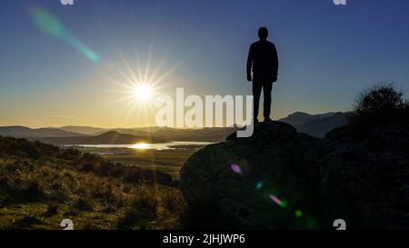 Man standing on a rock with his back facing the sunset over the mountains. Navacerrada Madrid. Spain. Stock Photo