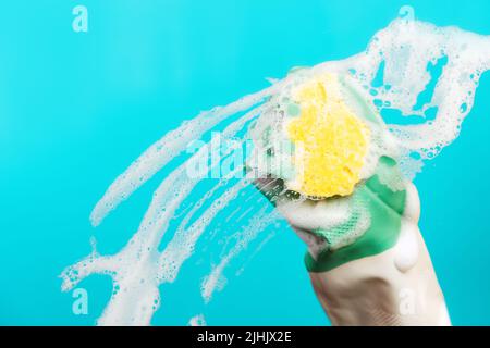 Close up of hand in rubber gloves wipes the glass with a foam sponge. Blue background with copy space. The concept of professional cleaning service. Stock Photo