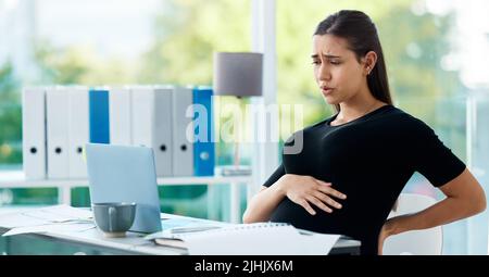 Overworked and in pain. a pregnant businesswoman experiencing pain while working in an office. Stock Photo