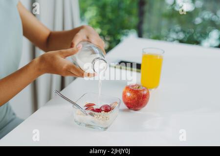 A young woman pours milk into a bowl with granola Stock Photo