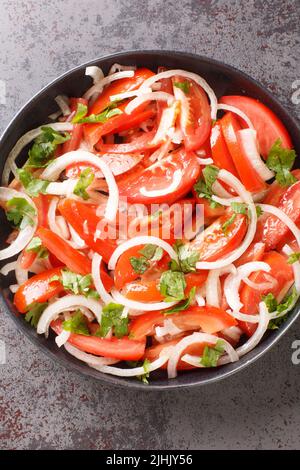 Ensalada chilena is a Chilean salad consisting of tomatoes, onions, olive oil, and coriander closeup in the plate on the table. Vertical top view from Stock Photo