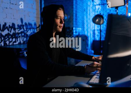 Side view of male hacker wearing hoods hacking to steal important information using computer to release malware viruses Ransom and harass Stock Photo