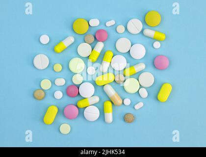 Pills of different sizes and colors on a blue background. Capsules and tablets colored top view. Dietary supplements of various types. Stock Photo