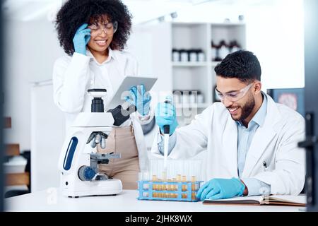 Two mixed race scientists wearing safety equipment while conducting medical research experiments with pipette and test tubes in a lab. Colleagues Stock Photo