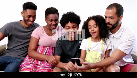 Happy African interracial family holding smartphone. Parents and kids looking at cellphone at home sofa Stock Photo