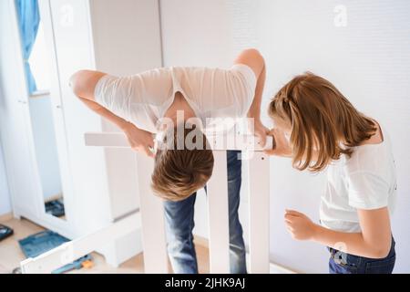 Dad,little girls daughters assemblle wooden baby bed according to instructions in kids room. Helping father, mounting children's furniture. Self-assem Stock Photo