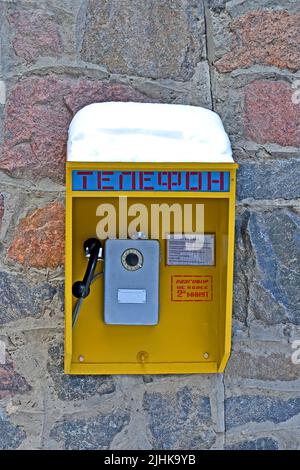 vintage soviet street telephone cabin on the stone wall under snow, retro wired technology diversity Stock Photo