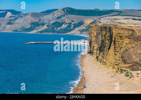 Dorset, England, United Kingdom, 19th July 2022. UK Weather: heatwave. A sea breeze makes the temperature bearable on the hottest day of the year along the Jurassic coast. A view of people walking under the precarious cliffs at high tide at Burton Freshwater, despite warnings not to after recent rockfalls Stock Photo