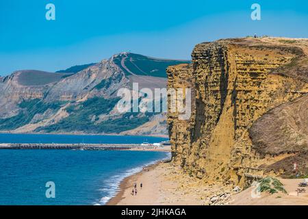 Dorset, England, United Kingdom, 19th July 2022. UK Weather: heatwave. A sea breeze makes the temperature bearable on the hottest day of the year along the Jurassic coast. A view of people walking under the precarious cliffs at high tide at Burton Freshwater, despite warnings not to after recent rockfalls Stock Photo