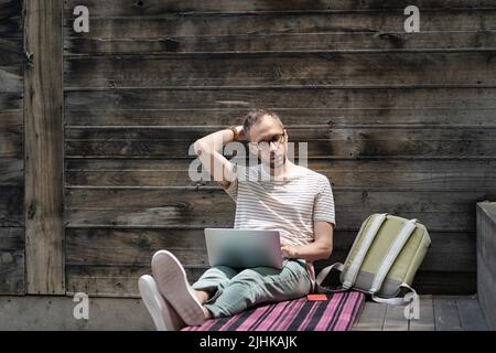 Focused man remote worker in eyewear working on laptop remotely outside. Outdoor workspace Stock Photo