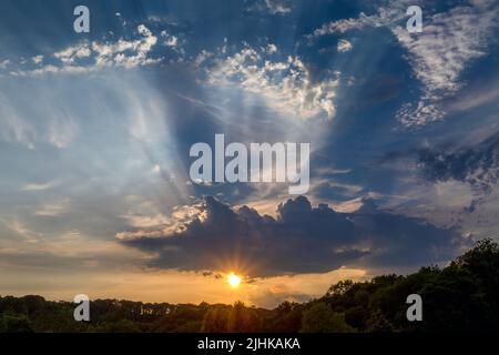 Sun rays bursting from behind the clouds over a forest in South Wales UK Stock Photo