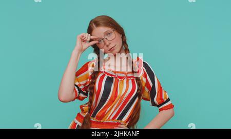 Need some more please give me. Girl showing a little bit gesture with sceptic smile, showing minimum sign, measuring small size, asking for help. Ginger teenager child kid on blue studio background Stock Photo