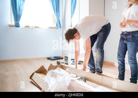 Dad,little girls daughters assemblle wooden baby bed according to instructions in kids room. Helping father, mounting children's furniture. Self-assem Stock Photo