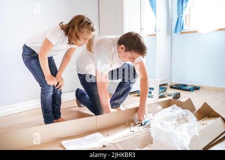 Dad,little girls daughters assemblle wooden baby bed according to instructions in kids room. Helping father, mounting children's furniture. Self-assem Stock Photo