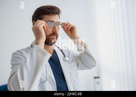 Professional doctor wearing glasses standing in medicine clinic hall and looking away Stock Photo