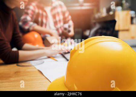 Close up image of a helmet on the desk with architects working with a laptop in the backward, an architectural concept Stock Photo