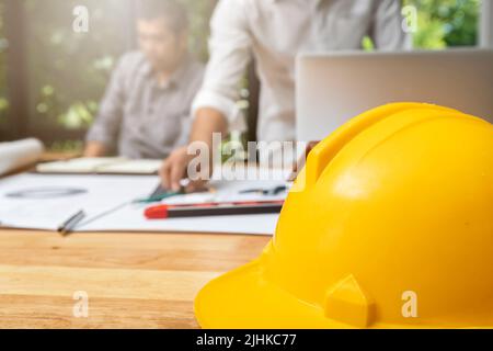 Close up image of a helmet on the desk with architects working with blueprint construction project, architectural concept. Stock Photo