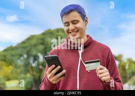 Latin gay man using credit card to make online payment on smartphone. Mixed race man using cellphone for shopping online. Guy using smart phone to che Stock Photo