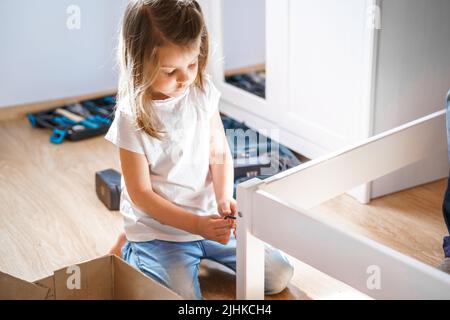 Dad,little girls daughters assemblle wooden baby bed according to instructions in kids room. Helping father, mounting children's furniture. Self-assem Stock Photo