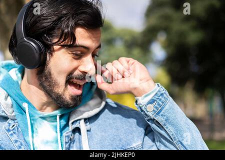 Young latin man listening to music outdoors with headphones. Expression of happiness, winning attitude. Stock Photo