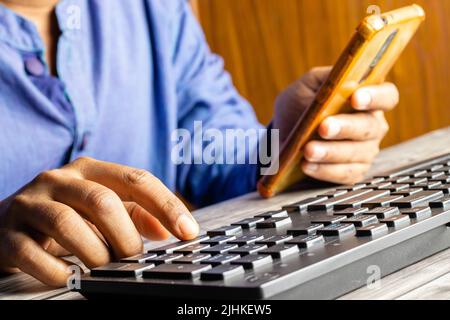 Selective focus on an Indian male hand using mobile phone to enter one time password in front of computer Stock Photo