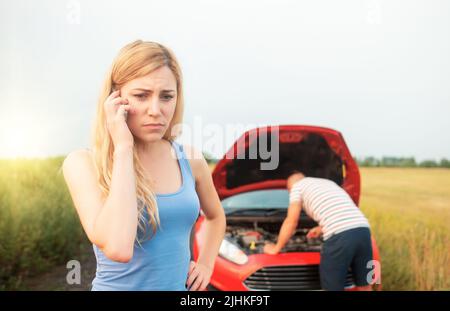 A young couple is trying to call for help in a car breakdown. Stock Photo
