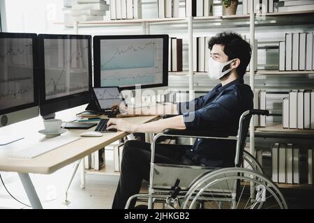 oung disabled businessman wearing face mask in wheelchair working on computer in office Stock Photo