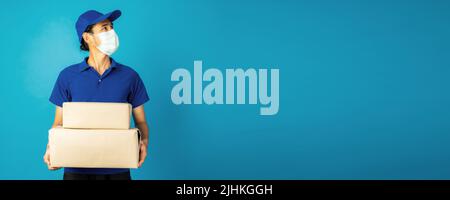 Portrait of excited delivery man in blue uniform holding parcel box isolated over blue background Stock Photo