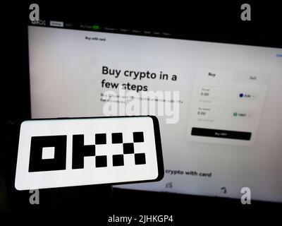 Person holding smartphone with logo of crypto company Aux Cayes FinTech Co. Ltd. (OKX) on screen in front of website. Focus on phone display. Stock Photo