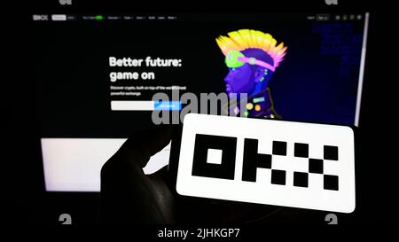 Person holding mobile phone with logo of crypto company Aux Cayes FinTech Co. Ltd. (OKX) on screen in front of web page. Focus on phone display. Stock Photo