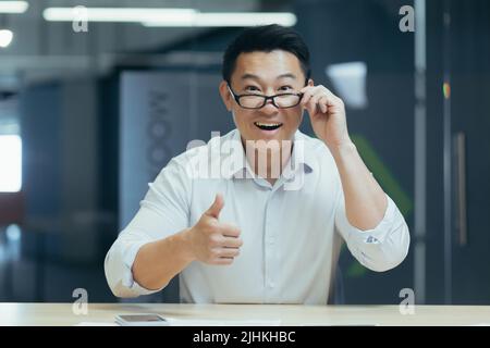 surprised asian man shoots glasses shocked looking at camera. Happy smiling rejoices. Look at monitor screen webcam view. amazed close up portrait. Face Handsome man Office worker wow expression Stock Photo