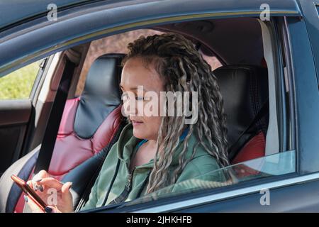 Attractive middle aged Asian woman sitting in a car and using the smartphone. Stock Photo
