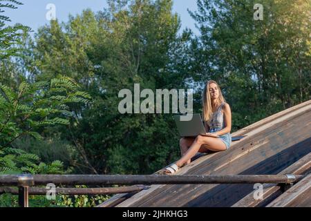Young woman with eyes closed and sunlight on her face enjoying working outdoors on her laptop in natural enviroment Stock Photo
