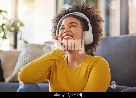 Young cheerful mixed race woman thinking while wearing headphones and listening to music at home. One content hispanic female with a curly afro Stock Photo