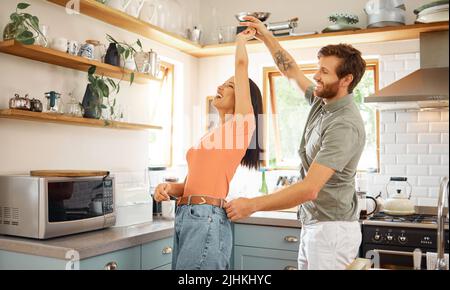 Young content interracial couple dancing in the kitchen at home. Playful caucasian boyfriend and mixed race girlfriend having fun. Husband and wife Stock Photo