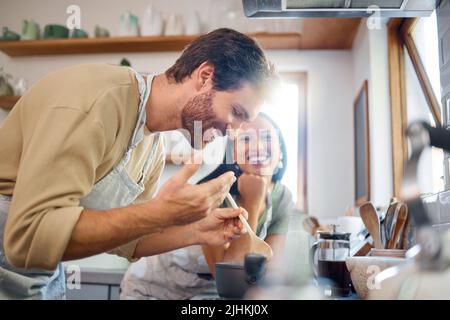 Happy young interracial couple standing by the stove while cooking together in the kitchen at home. Young caucasian man looking and smelling steamy Stock Photo