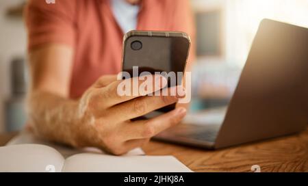 Man using a phone while working from home alone. One businessperson working on a laptop and writing in a notebook while using social media on a Stock Photo