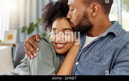 Young happy mixed race boyfriend kissing his girlfriend on the forehead while relaxing at home. Cozy hispanic husband and wife smiling while hugging Stock Photo