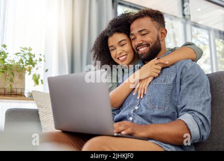 Young happy mixed race couple smiling while using a laptop together at home. Joyful hispanic boyfriend and girlfriend relaxing and using a laptop in Stock Photo