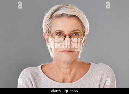 One mature caucasian woman wearing trendy brown prescription spectacles against a grey copyspace studio background. Senior female looking serious Stock Photo