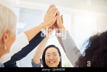 Group of diverse businesspeople giving each other a high five while standing together in a huddle in an office. Ambitious colleagues staying motivated Stock Photo