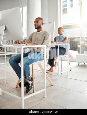Young serious african american businessman using a desktop computer in an office at work. Focused male businessperson typing an email at a desk Stock Photo