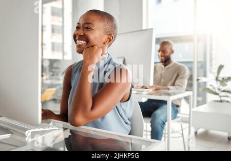Young joyful african american businesswoman using a desktop computer in an office at work. Cheerful black female businessperson reading an email at a Stock Photo