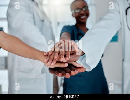Group of diverse doctors stacking their hands together in support while working at a hospital. Medical professionals joining their hands in unity and Stock Photo