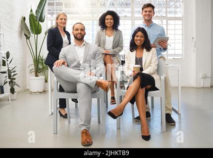 Portrait of a group of five cheerful diverse businesspeople sitting together at work. Business professionals having a meeting in an office. Colleagues Stock Photo
