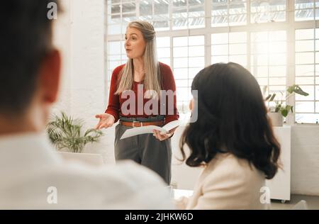 Mature boss talking to staff in a meeting. Leading businesswoman collaborating with staff.Powerful businesswoman leading a meeting. Senior architect Stock Photo