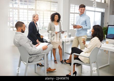 Group of five diverse businesspeople having a meeting in an office at work. Cheerful coworkers laughing together in a workshop. Business professionals Stock Photo