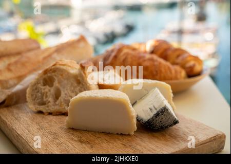 Sunny morning in Provence, breakfast with fresh baked croissant, baquett bread, crottin goat cheese and view on fisherman's boats in harbour of Cassis Stock Photo
